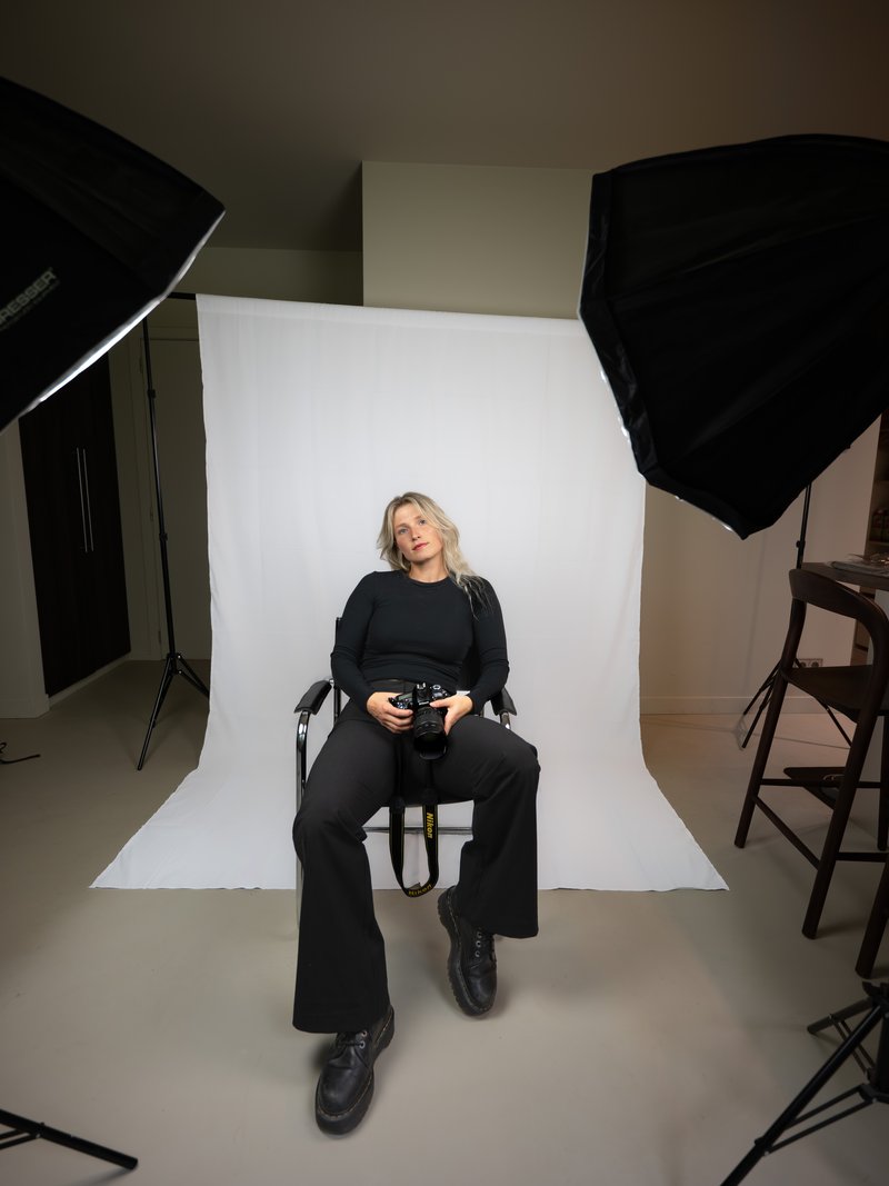 Indra Janssens zittend met haar camera in de studio, softboxen aan weerszijden van een witte achtergrond